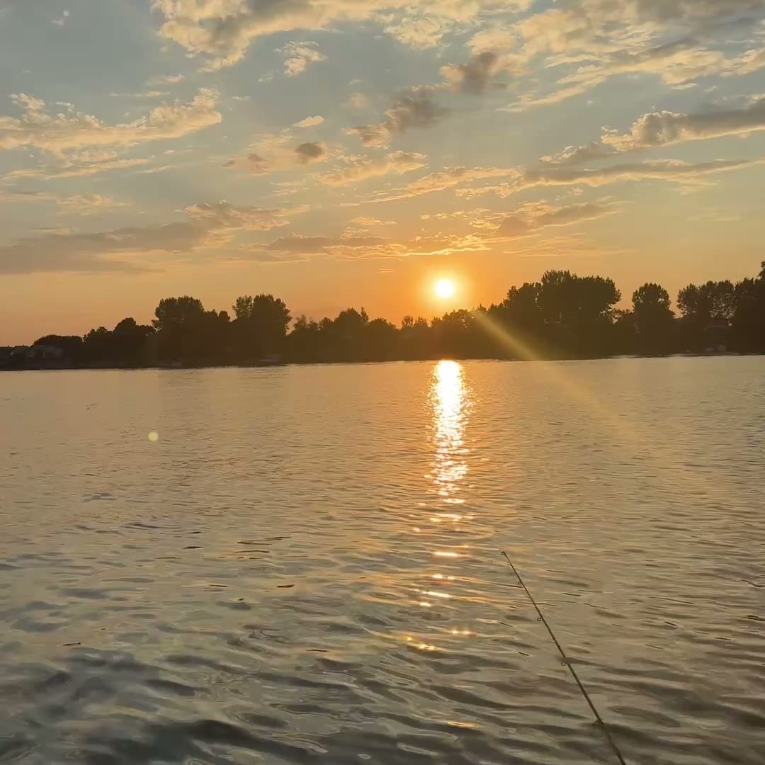 Zalazak sunca nad rekom sa štapom za pecanje u čamcu